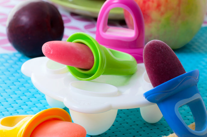 Nuby Fruitsicles Ice Pop Tray on a table next to an apple, plum, and some grapes.