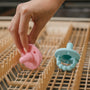A pink and blue Nuby Silicone Softees Pacifier being placed on the top rack of a dishwasher.
