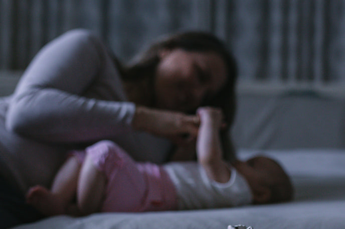 Blurry photo of a smiling mother and infant playing on a bed.