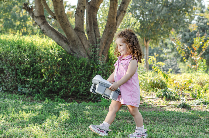 Toddler carrying a Nuby On-the-Go Portable Potty Seat while outside.