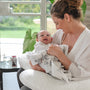 Smiling mother wearing white holding her infant child in a zebra blanket on a nursing pillow.