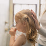 Toddler girl brushing her teeth with her mother's hand resting gently on the back of her head.