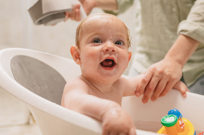 Baby getting bathed in a Nuby Sit and Bathe Compact Bathtub, playing with Tub Tugs bath toys.