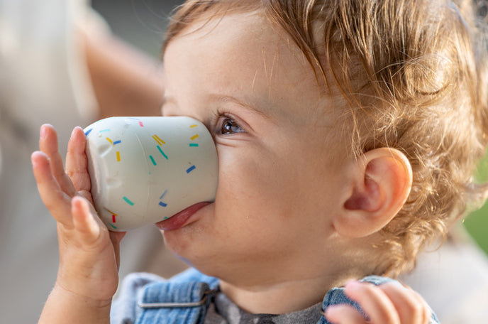 A toddler drinking from his Baby's First Mini Sipper Training Cup by Nuby.