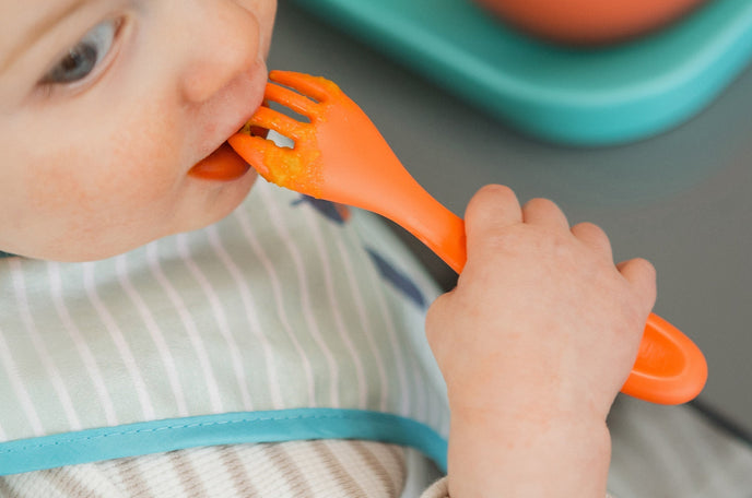 Toddler eating at mealtime using an orange Nuby fork.