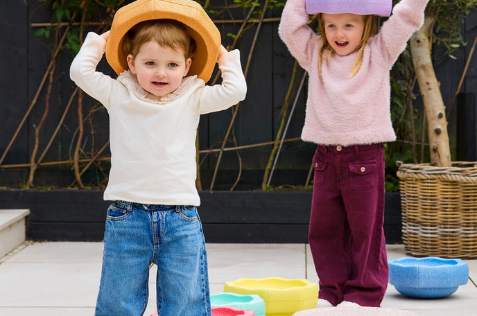 Two children playing with Nuby StepPebble stepping stones on their heads, while outside.