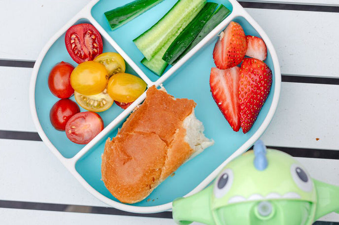 Nuby Rectangular Silicone Suction Plate in aqua holding fruits and vegetables, next to a Dino Clik-It Silicone Straw Trainer Cup.