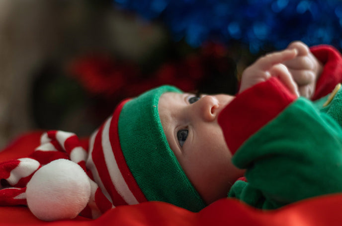 An infant wearing green and Christmas-themed hat with red and white stripes.