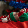 An infant wearing green and Christmas-themed hat with red and white stripes.