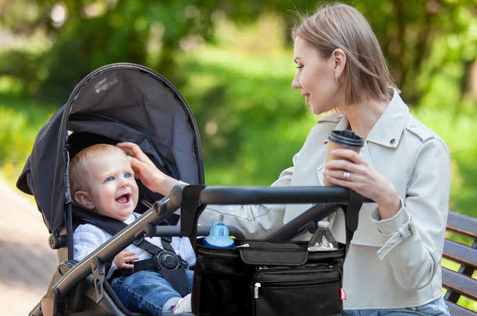 Mother on park bench playing with her baby who is laughing in a stroller.