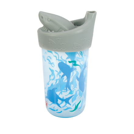 The Nuby 3D Character Soft Spout Sippy Cup | Grey Shark features a blue cup with a gray shark-shaped lid, silicone spout, and fun shark and seaweed illustrations—perfect for little ocean explorers and designed to resist leaks.