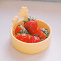 Four fresh strawberries in the Nuby Animal Friends All Silicone Bowl, featuring two giraffe-shaped handles. This yellow baby dinnerware is perfect for self-feeding and sits on a light-colored surface.