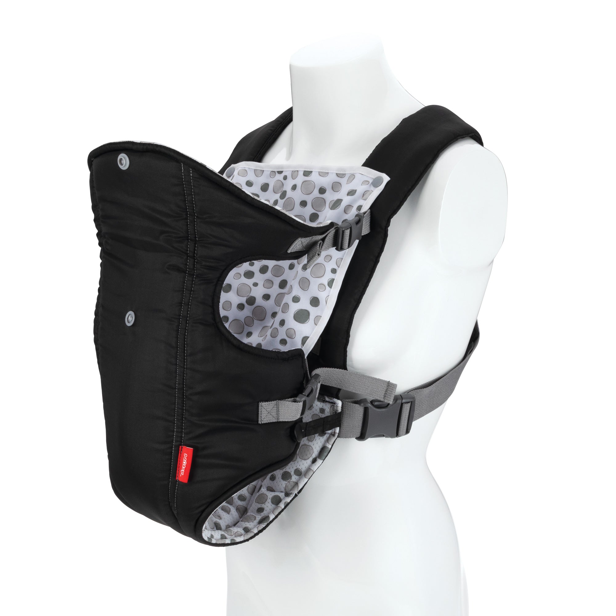 The Nuby Classic Baby Carrier | Black is shown on a white mannequin torso, featuring gray straps, a polka dot interior, side buckles, and padded shoulder straps for comfort. Suitable for newborns to toddlers.