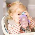 A young blonde child in a striped shirt with a red hair clip sits in a high chair, drinking from the 2-in-1 Toddler Cup (2 Pack) | Tiger & Rainbows.