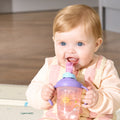 A baby with blonde hair and blue eyes smiles while drinking from a 2-in-1 Toddler Cup (2 Pack) | Tiger & Rainbows, featuring a weighted straw and colorful tiger and rainbow designs.