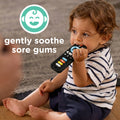 A toddler in a striped shirt sits on a rug, chewing on the Silicone Remote Control Teether Toy. Text reads: Gently soothe sore gums next to a smiling baby icon.