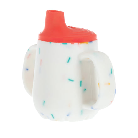 The Nuby US 2-Handle First Training Cup in Red Confetti features a white cup with colorful specks, two large side handles, and a red free-flow spout lid.