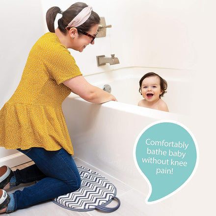 A woman kneels on a Folding Bathtub Kneeling Pad by the tub, smiling at a baby. A speech bubble says, Comfortably bathe baby without knee pain!.