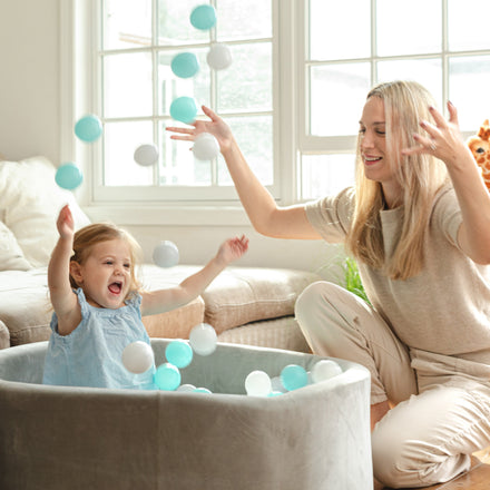 A smiling woman and a young girl toss balls together in the Kids' Ball Pit for Home with 200 Balls | Aqua, enjoying playtime in a bright living room.