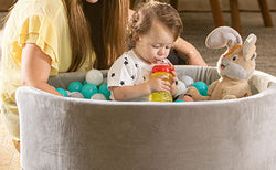 Mother sitting outside a Nuby Kids' Ball Pit (Aqua). A toddler sits inside, sipping from a Nuby Flex Straw Leakproof Sippy Cup.