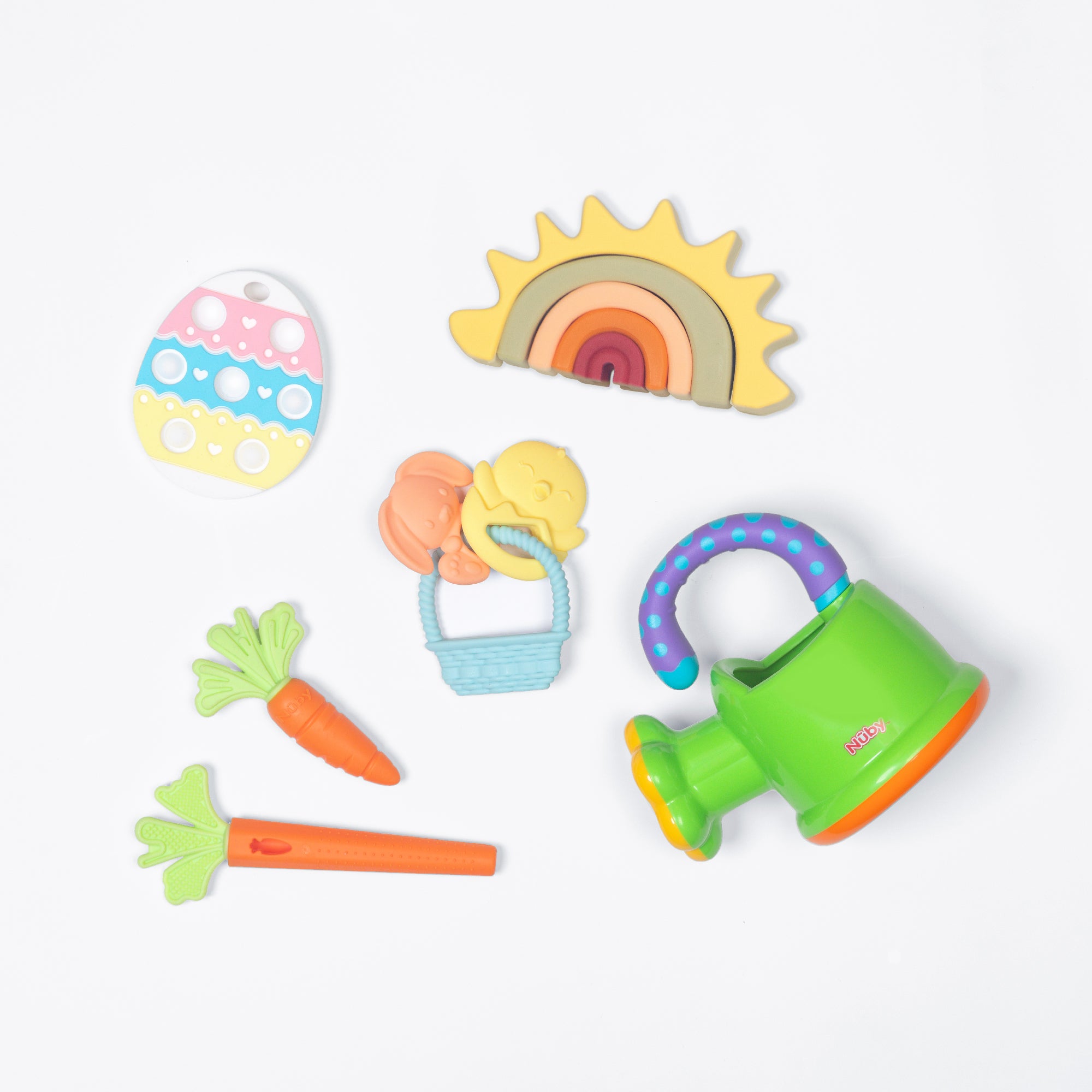 The Nuby US One & Done Bunny Basket Bundle features colorful sensory toys: a green watering can, two orange carrots, a rainbow, an egg-shaped toy, and an Easter basket with a bunny and chick—perfect for playtime.