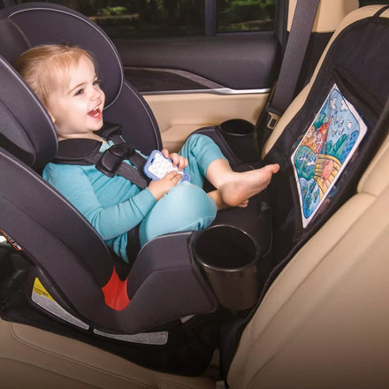 A smiling toddler sits in a rear-facing car seat, holding a toy and looking at a colorful drawing, protected by the Nuby Safe in the Seat Car Seat Protector.
