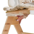 A hand adjusts a bolt on the side of the Grow with Me Foldable High Chair, which features a padded seat.