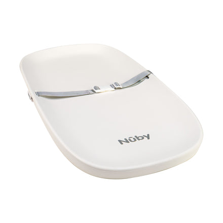The Changing Pad is white with a contoured shape, non-slip base, and grey safety harness across the middle. The Nûby brand name is printed near the bottom.