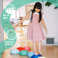 A young girl in a pink dress balances barefoot on StepPebbles and a FREE Balance Board | Pastel indoors. Icons show "For all ages" and "Cognitive growth," highlighting the learning benefits of these indoor-outdoor kids’ balance toys.