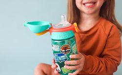 Young, smiling girl wearing an orange sweatshirt sitting with a Nuby leakproof water bottle.