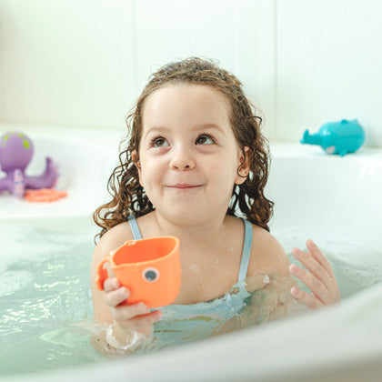 Toddler in bathtub, holding a Nuby bath toy.