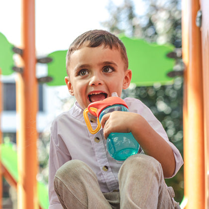 Boy drinking from blue and orange Nuby sippy cup.