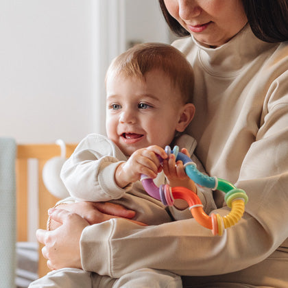 Infant in mother’s arms, playing with Nuby teether.