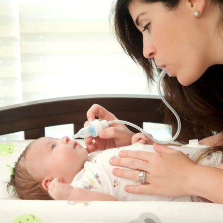 A woman uses the Nuby Breathe-eez Nasal Aspirator with a tube to help relieve her baby's congestion as the baby lies on a changing table, looking up at her.