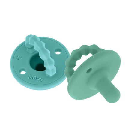 The Nuby Silicone Softees Pacifier & Teether (2 Pack) includes two teal silicone pacifiers with circular shields and textured handles for easy grip. One pacifier doubles as a teether and features the Nuby logo embossed on the front.