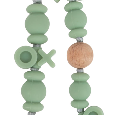 Close-up of the Nuby Silicone and Wood Beaded Pacifier Clip, featuring matte green silicone and wooden beads with O and X tic-tac-toe shapes, all strung on a gray cord.