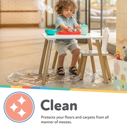 A young child eats at a small table atop the Nuby No-Mess Mealtime Floor Mat, protecting floors and carpets from spills. Text reads: Clean. Shields your surfaces from all kinds of mealtime messes.