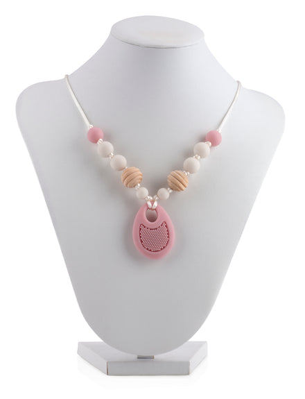 The Nuby Silicone Teething Necklace features white and pink round beads, wooden-textured accents, and a pink teardrop pendant with mesh detail, displayed on a white stand.